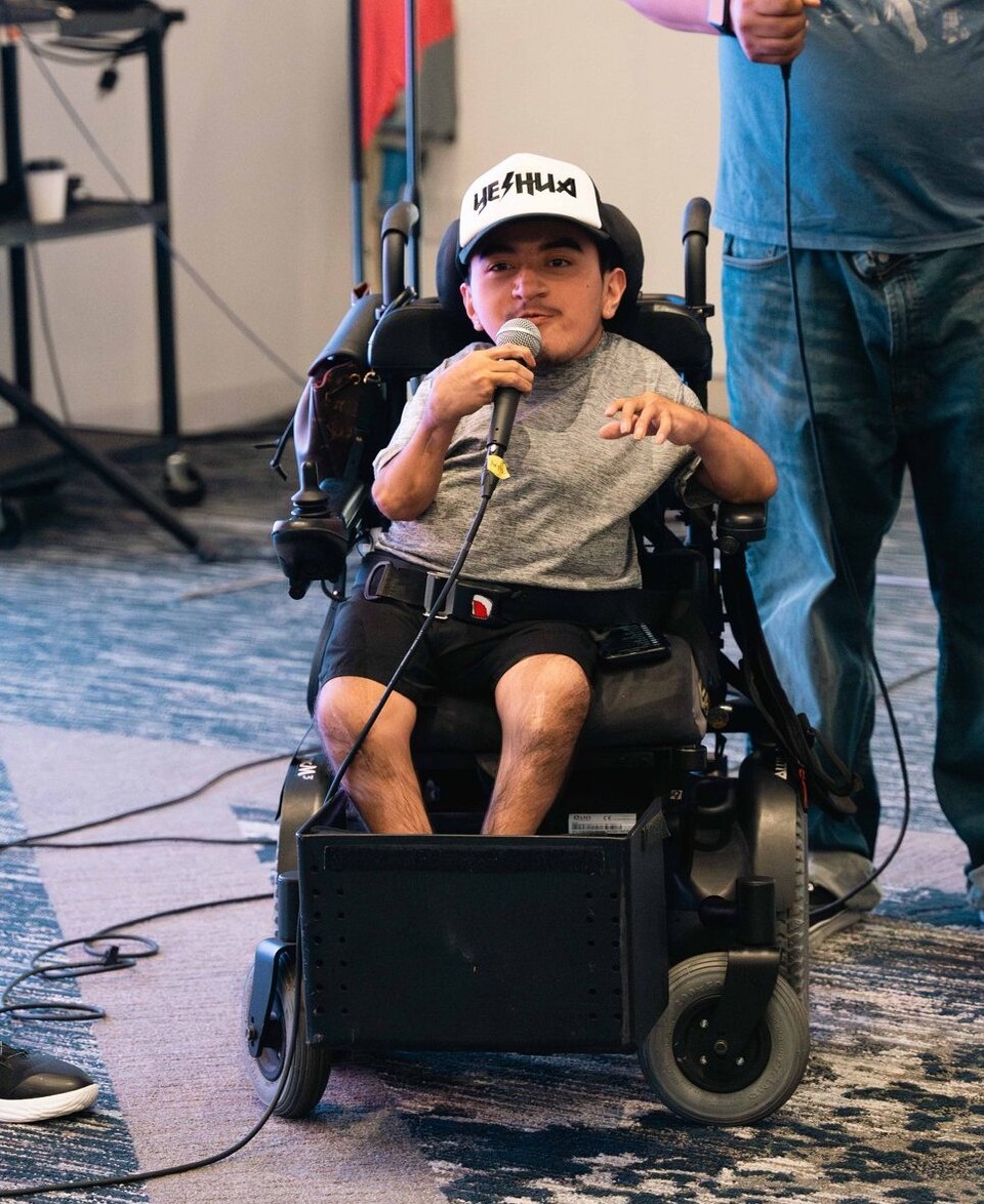 Isaac Immanuel holding a handheld mic in a white "Yeshua" cap
